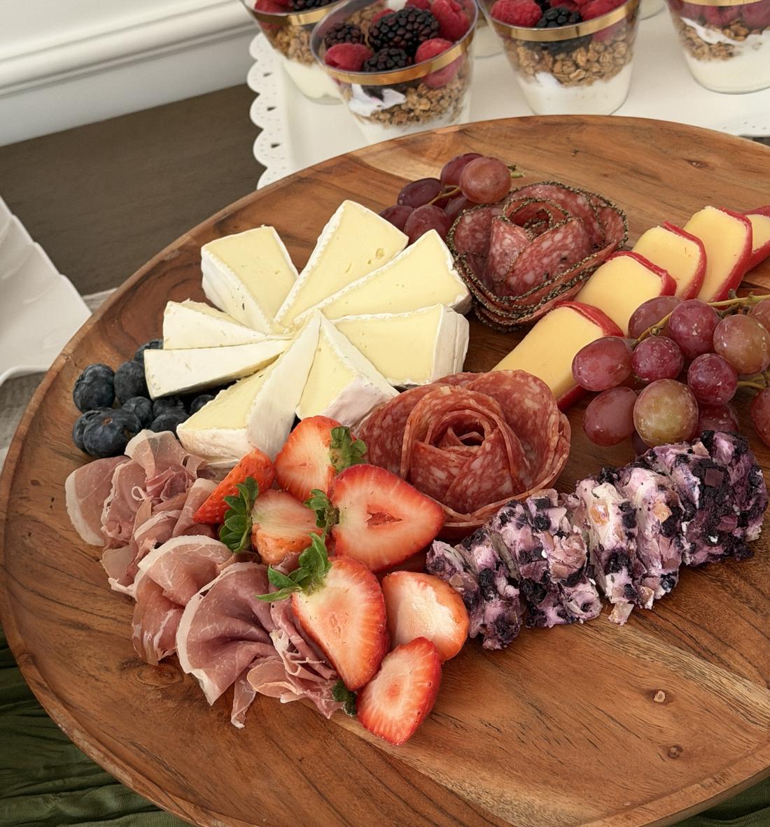 Round wooden board with brie, salami rose, prosciutto, strawberries and blueberry goat cheese